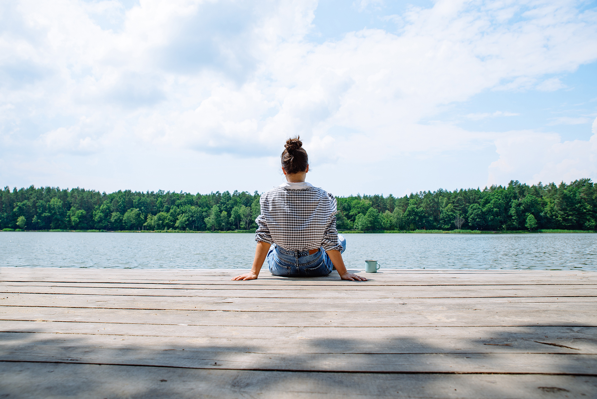 woman sitting on wooden dock looking at lake in sunny day